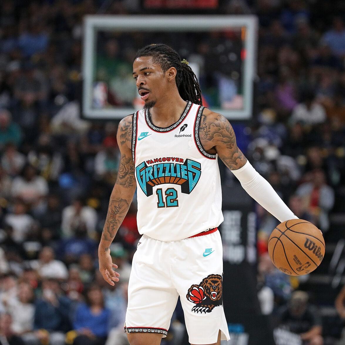 Ja Morant in a white jersey with a "Grizzlies" written in cerulean blue across the chest, the number 12 below it, holding a basketball in his left hand with a hoop in the distance.